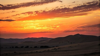 Fototapeta premium A breathtaking desert sunset with vibrant orange and red hues. The sun sets behind rolling sand dunes, casting long shadows.