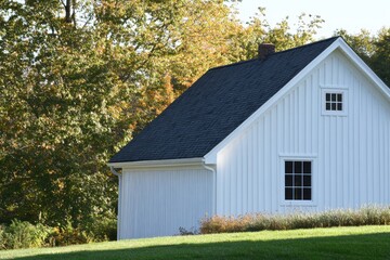 Obraz premium White cottage nestled in greenery with a clear blue sky above, surrounded by vibrant autumn trees in a serene landscape during early afternoon