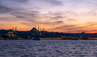 High resolution panoramic photograph capturing Istanbul's historic peninsula bathed in a crimson sunset glow. The city's iconic skyline silhouettes against the vibrant evening sky