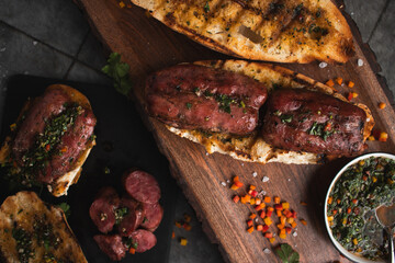 A choripan with chimichurri sauce on a wooden board. Traditional argentinian sandwich. 