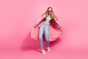 Trendy young woman wearing shiny top and pink jacket posing in colorful studio