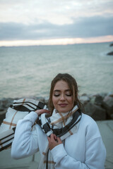 Fototapeta premium Beautiful young girl in a white tracksuit stands on the seashore in stormy weather