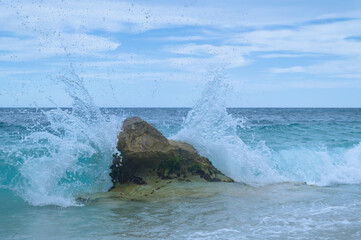 This image captures an ocean wave crashing against a rock, with water.