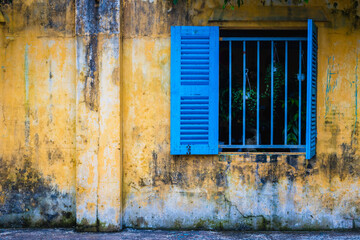 Weathered yellow wall with blue shuttered window