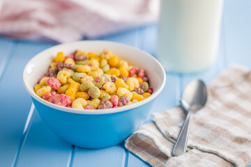 Colorful breakfast cereals in the shape of various fruit in bowl on blue table.