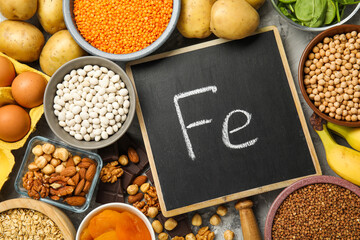 Diet plan for anemia. Different products rich in iron and small chalkboard with Ferrum symbol on grey table, flat lay. Space for text