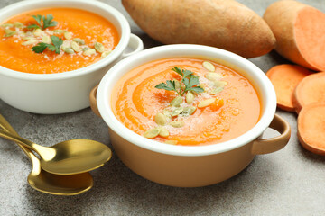 Delicious sweet potato soup with pumpkin seeds in bowls and fresh vegetables on grey textured table, closeup