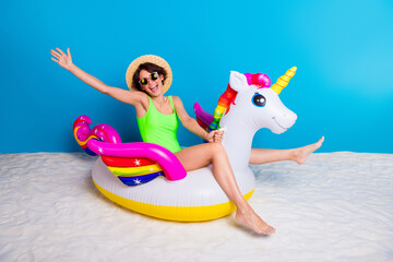 Excited Young Woman Posing With Colorful Unicorn Float Toy on Sandy Beach With Blue Background