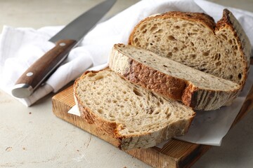 Cut loaf of fresh bread and knife on table, closeup