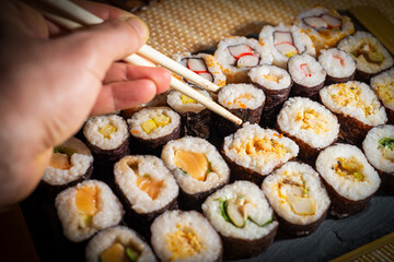 Taking sushi roll with chopsticks from the slate serving tray