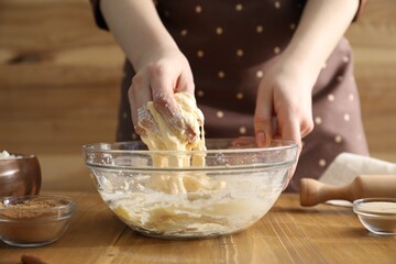 Woman kneading dough for cinnamon rolls at wooden table, closeup