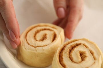 Woman putting cinnamon roll into baking dish, closeup