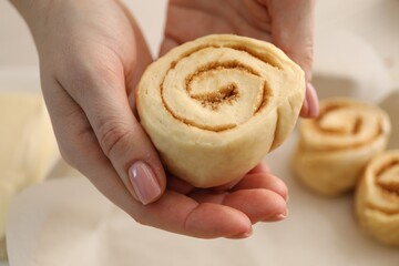 Woman with uncooked cinnamon roll at table, closeup