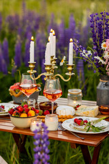 Perfect surprise date for loving couple, private wedding, romantic marriage proposal. Summer, sunset, golden hour. Appetisers. Beautiful elegant outdoor arrangement in meadow with purple blue lupins