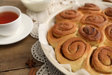 Freshly baked cinnamon rolls and tea on wooden table, closeup