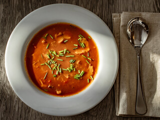 goulash soup in a white plate on a wooden table with a spoon
