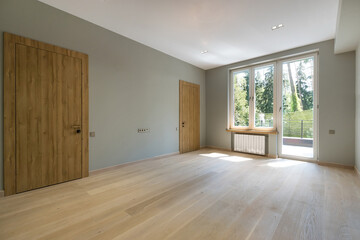 A room with a final finish in a private house. Unfurnished. Light laminate flooring, brown .doors and access to the balcony.