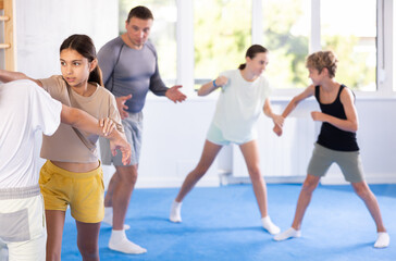 Boy and girl paired up and practice to aim stroke to neutralize opponent and repulse attack. Class self-defense training in presence of experienced instructor