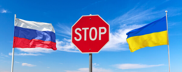 Stop Russian invasion concept. Red stop traffic regulatory warning sign between waving Russian and Ukraine flags against blue sky with clouds