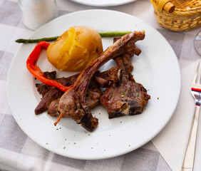 Appetizing fried lamb ribs served on platter with potatoes and peppers