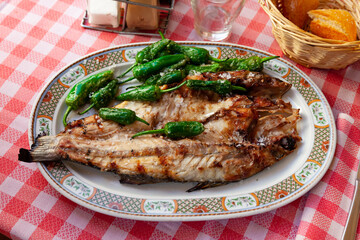 Grilled sea bass fish with green peppers on platter on plaid tablecloth