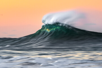 A vibrant wave captured with motion blur, showcasing its dynamic flow and energy against a soft pastel sky. Taken in Australia.
