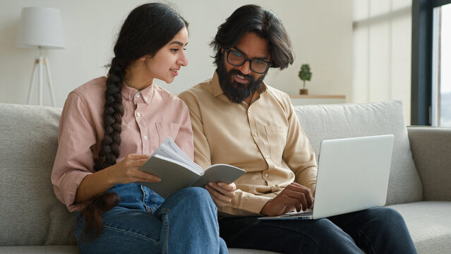 Multiracial couple Arabian Indian adult man and woman read paper notes pay bills loan mortgage business payment planning family budget diverse wife and husband use laptop check finances in living room - Powered by Adobe