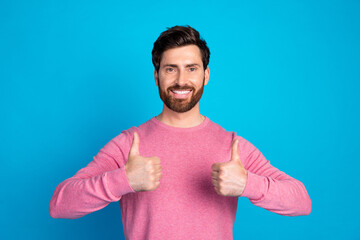 Fototapeta premium Young man in pink sweater giving thumbs up, expressing positive attitude against blue background