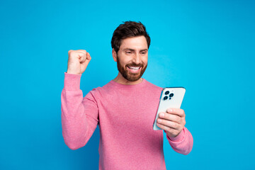 Cheerful man in pink sweater celebrating success with smartphone against vibrant blue background