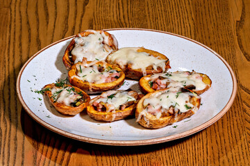A plate of baked potatoes topped with cheese and ham on a wooden table