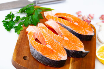 Raw salmon steaks, lemon, parsley and garlic on wooden background, home cooking