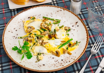 Scrambled eggs with mushrooms and asparagus served on plate with silverware.