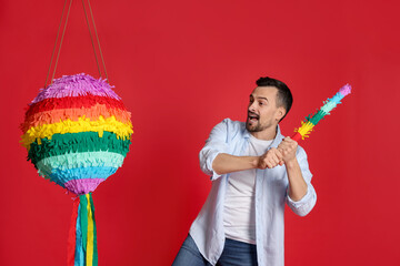 Happy man hitting colorful pinata with stick on red background