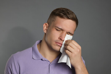 Crying man wiping tears with tissue on grey background