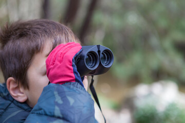 Child boy holds binoculars in nature