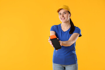 Happy courier with payment terminal on yellow background, space for text