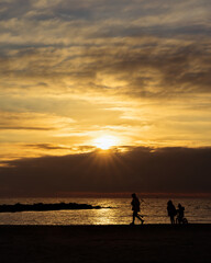 Silhouettes of People on the Beach at Sunset with Golden Sky and Calm Ocean