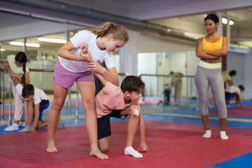 Group of kids exercising self-protection moves on group training. Trainer standing beside and watching them.