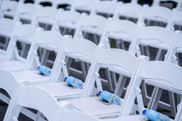 Outdoor Event Seating Rows of White Chairs with Water Bottles Chuppah seating arranged 