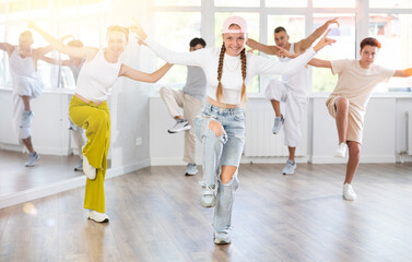 Happy teenage girl practicing hip-hop reject step in training hall during group dancing classes