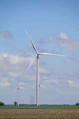 Giant white wind turbines in green field with white clouds and blue sky