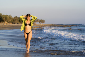 Young white woman in black bikini on the beach at sunset