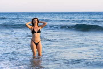 Young white woman in black bikini on the beach at sunset