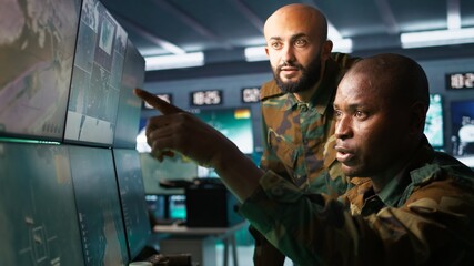 Army unit working in governmental facility next to colleague, operating surveillance monitoring tech with digital equipment. African american man doing job in base of operations, camera B
