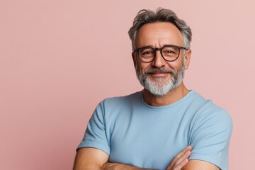 Fototapeta premium Smiling senior man with gray beard and glasses poses confidently against pink background