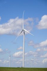Giant white wind turbine windmill with blue sky and cumulus clouds