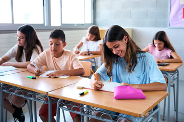 Happy Caucasian girl primary school student doing teacher lesson exercises in classroom. Nerdy female child sitting at desk studying in class. Young pre-adolescent kids, concept of primary education
