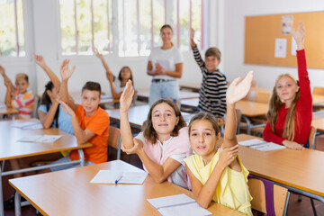 Group of active studious preteen pupils studying together in elementary school, raising hands to answer