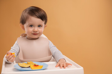 Healthy baby food. Cute little kid eating fruits in high chair on beige background, space for text