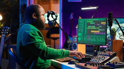 African american sound engineer using midi controller notes to add audio effects in post production, editing tracks with digital software and mixing console. Male musician in home studio. Camera A.
